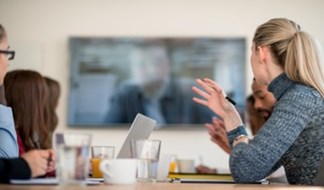 Boardroom of people talk to a man over video conferencing