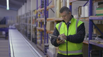 Man wearing hi-viz jacket working through a Health & Safety audit checklist in a warehouse.