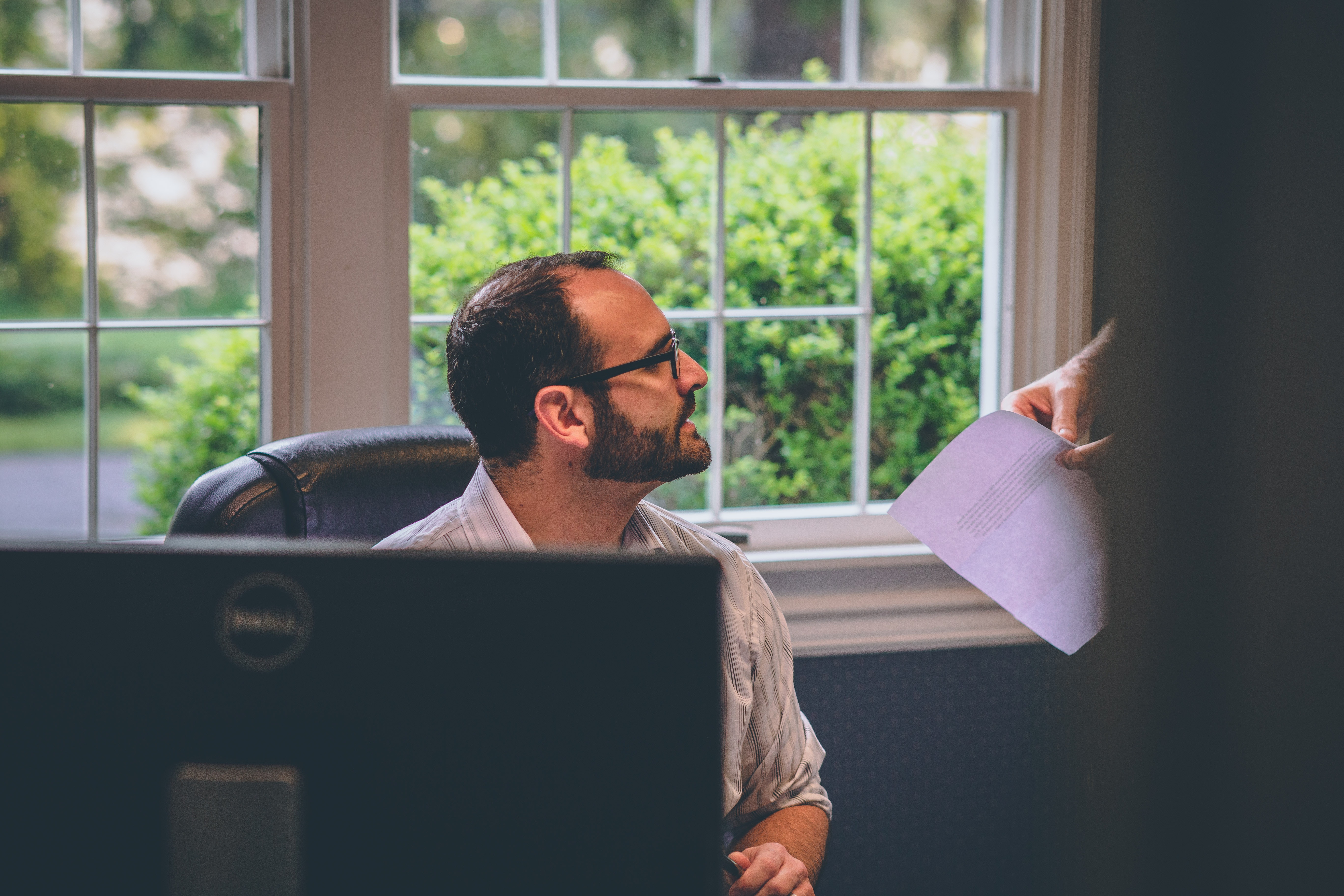 document being handed over to someone sitting in front of a computer