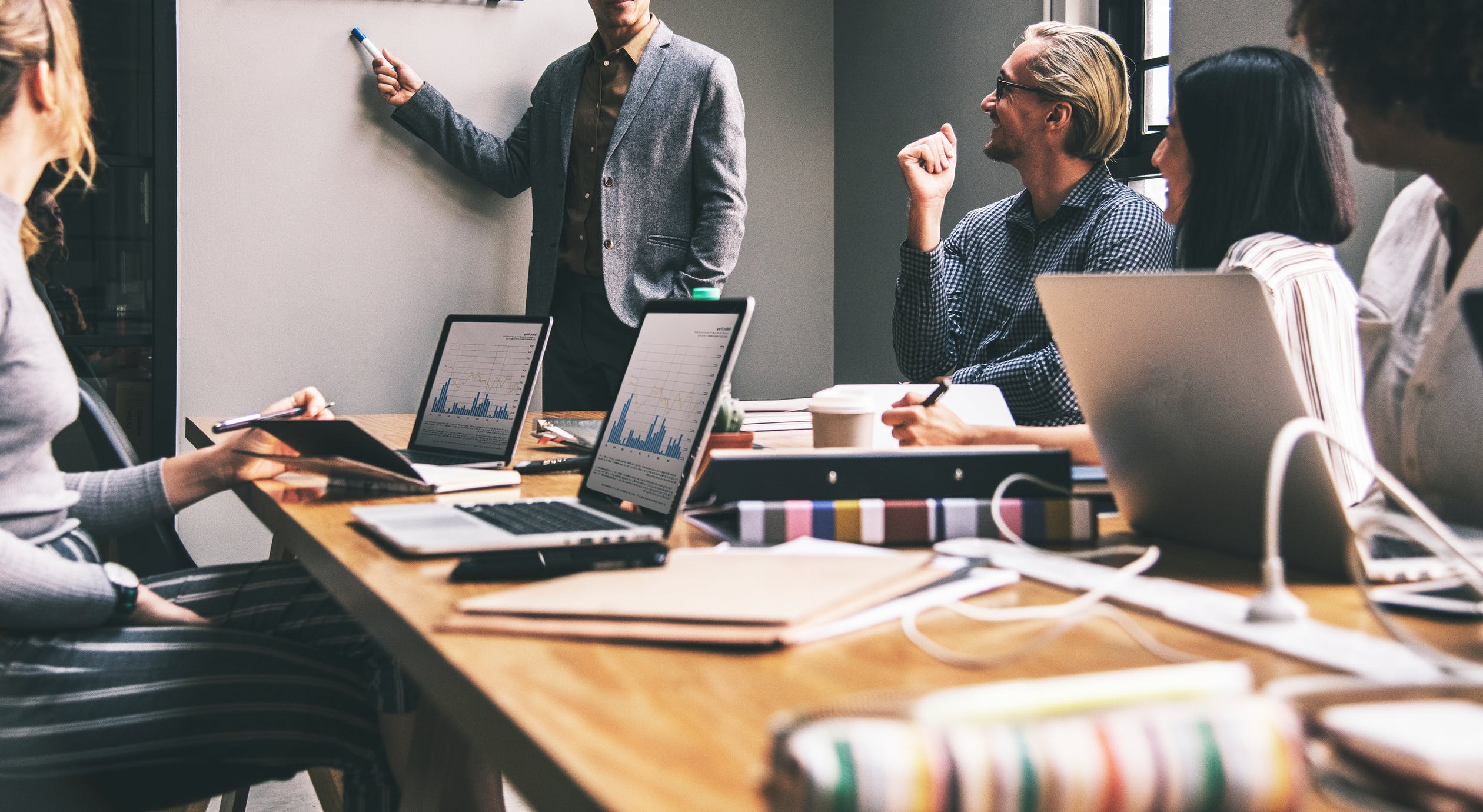 Man standing pointing at whiteboard, presenting to room of professionals