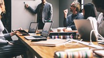 Man standing pointing at whiteboard, presenting to room of professionals