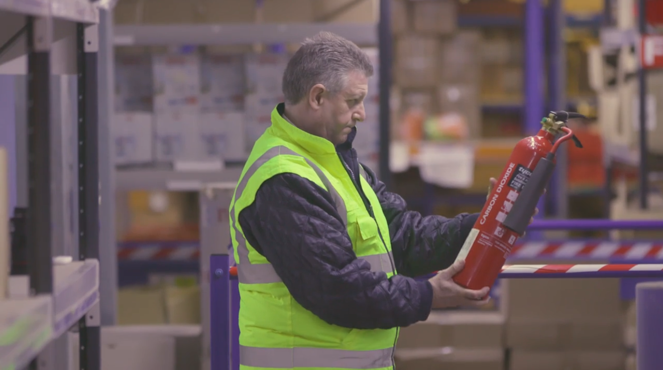 Paper on a table as 3 people discuss something in front of a whiteboard