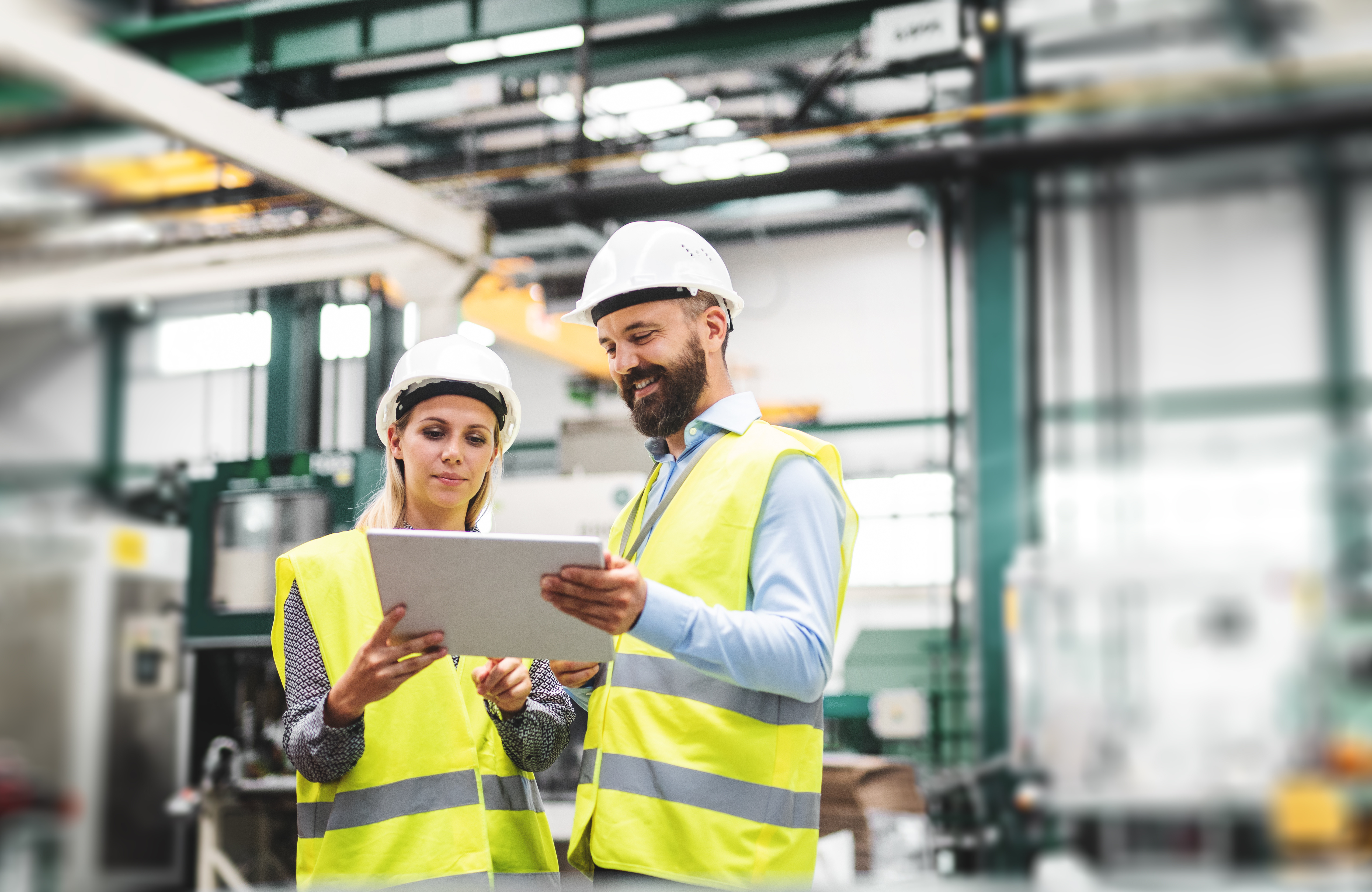 Man and woman in high viz reading from tablet, in a warehouse 