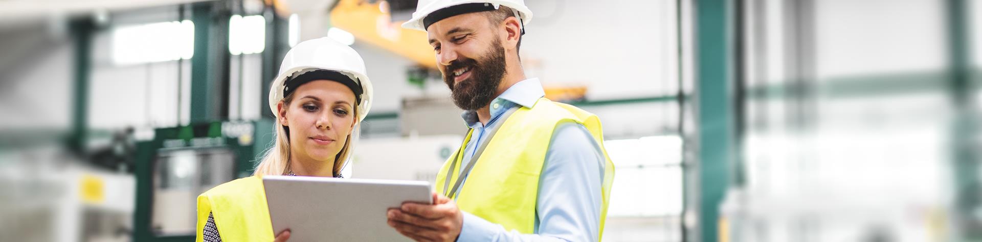Man and woman in high viz reading from tablet, in a warehouse